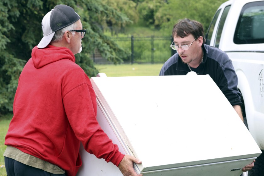 Two men carry a freezer.