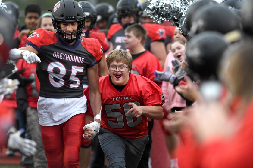 Duluth East’s Jackson Carlson (85) holds hands with William Hassebrock (58) of the Greyhounds’ adaptive football team, as Hassebrock gets announced before the game with Cloquet