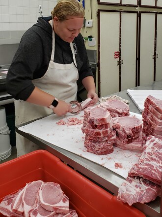 Woman processing pork chops in butcher shop
