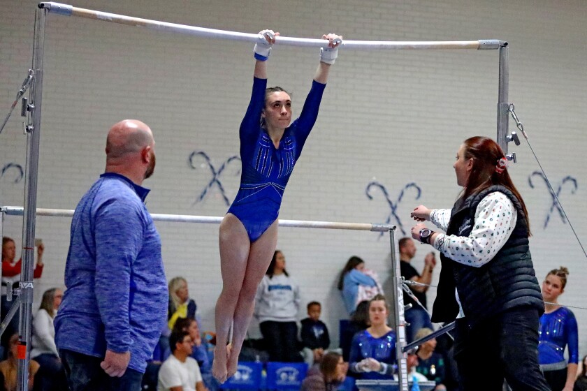 Coaches watch as a gymnast performs a bar routine.