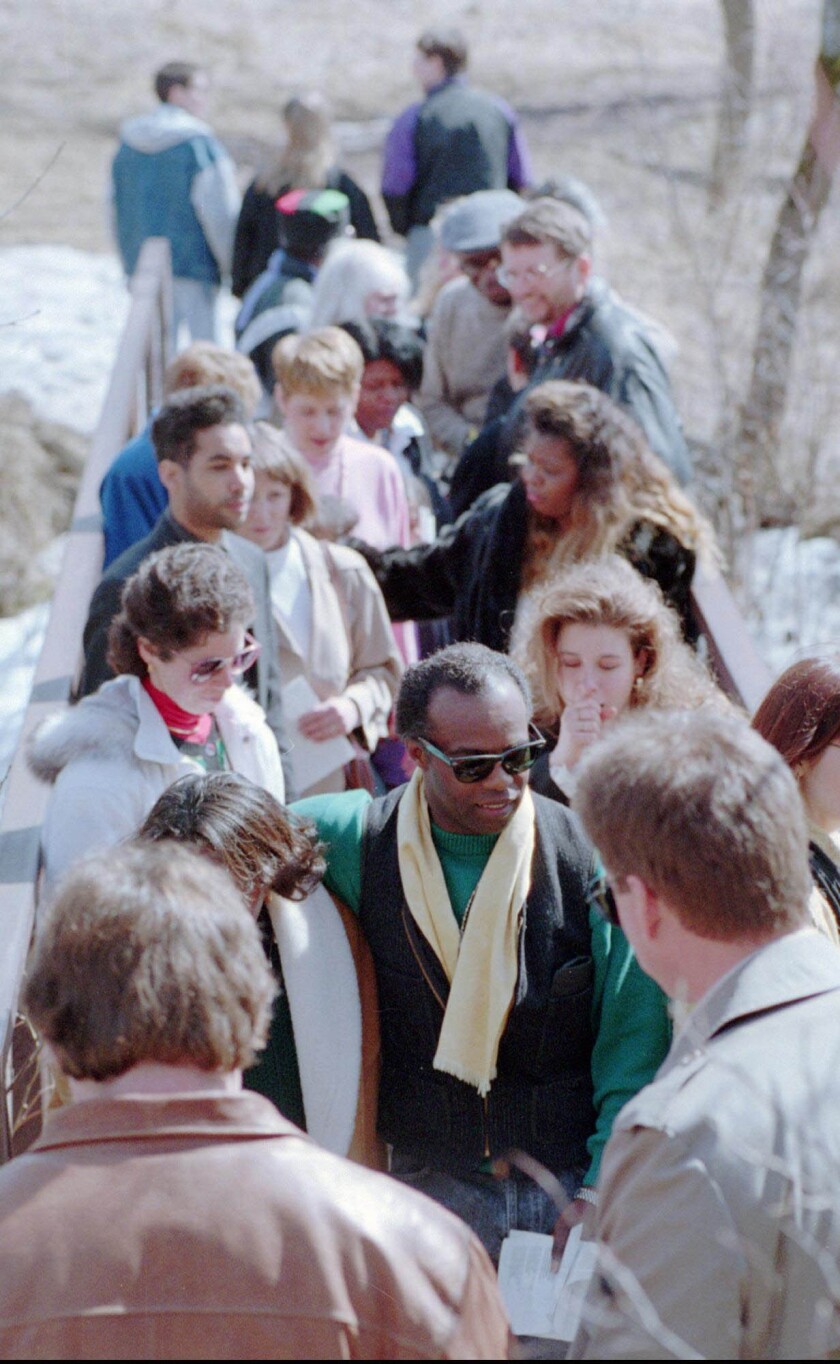 man surrounded by numerous funeral mourners on pedestrian bridge