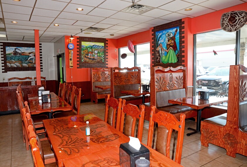 Wooden tables, chairs and booths sit inside the restaurant, with orange walls and brightly colored paintings