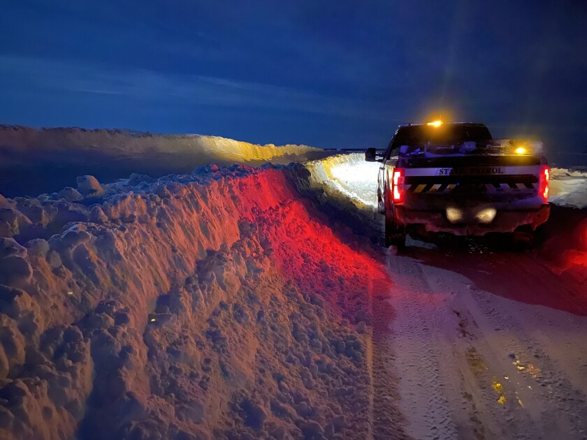 A truck drives down a road that is bordered by snow up to the side mirrors.