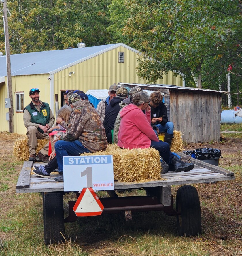 People sit on hay bales on a wagon.