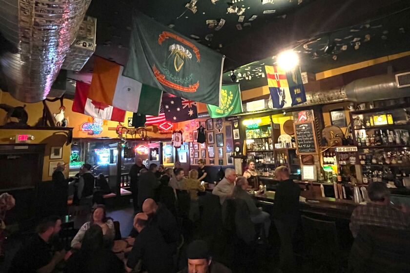 Interior of a moderately crowded pub, with several people sitting at the bar and a dozen or so more relaxing around tables.