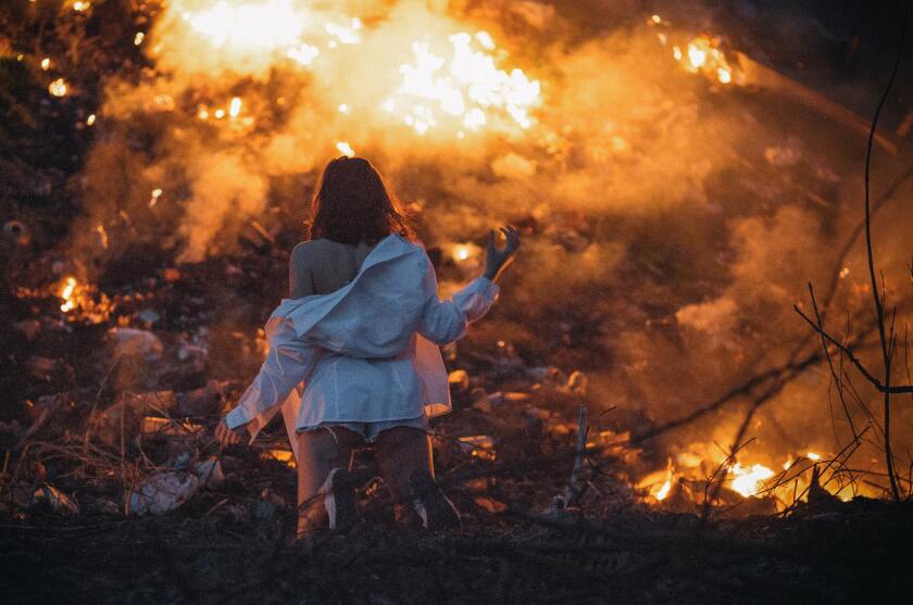 A female kneels before a destructive fire.