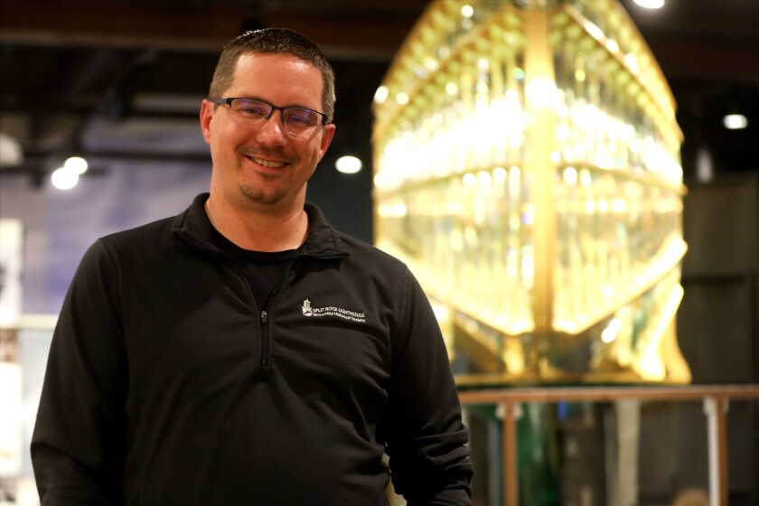 A man standing in front of a lit, replica lighthouse beacon.