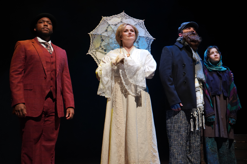 Four actors stand on stage: a young Black man in reddish suit, a young white woman in elegant white dress, and a white father and young daughter in humble but warm clothes.