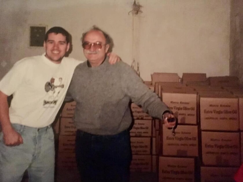 A young man poses and smiles with his arm around an older, smiling man.