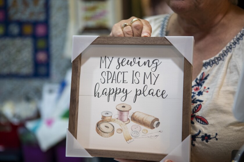 Paisley Threads owner Linda Lagergren holds a sign reading "My sewing space is my happy place" in her store, Paisley Threads, in New London on Thursday, July 28, 2022.