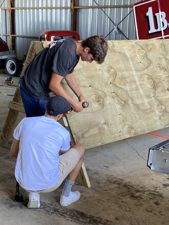 Sam Johnson, standing, and Marcus Salzwedel, kneeling, work together to build an obstacle for the TriForHealth Youth Obstacle Challenge, set to take place on July 30, 2022.