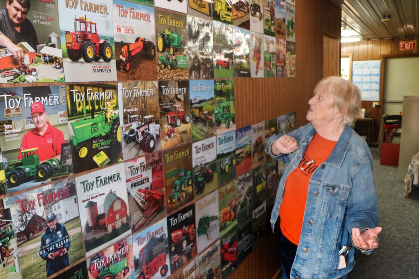 A woman in a blue jean jacket and a red Toy Farmer T-shirt reviews a number of monthly magazine covers on display in a hallway at the magazine's offices.