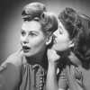 two light-skinned women with elaborate bobby-pinned updos gossip in black and white photo