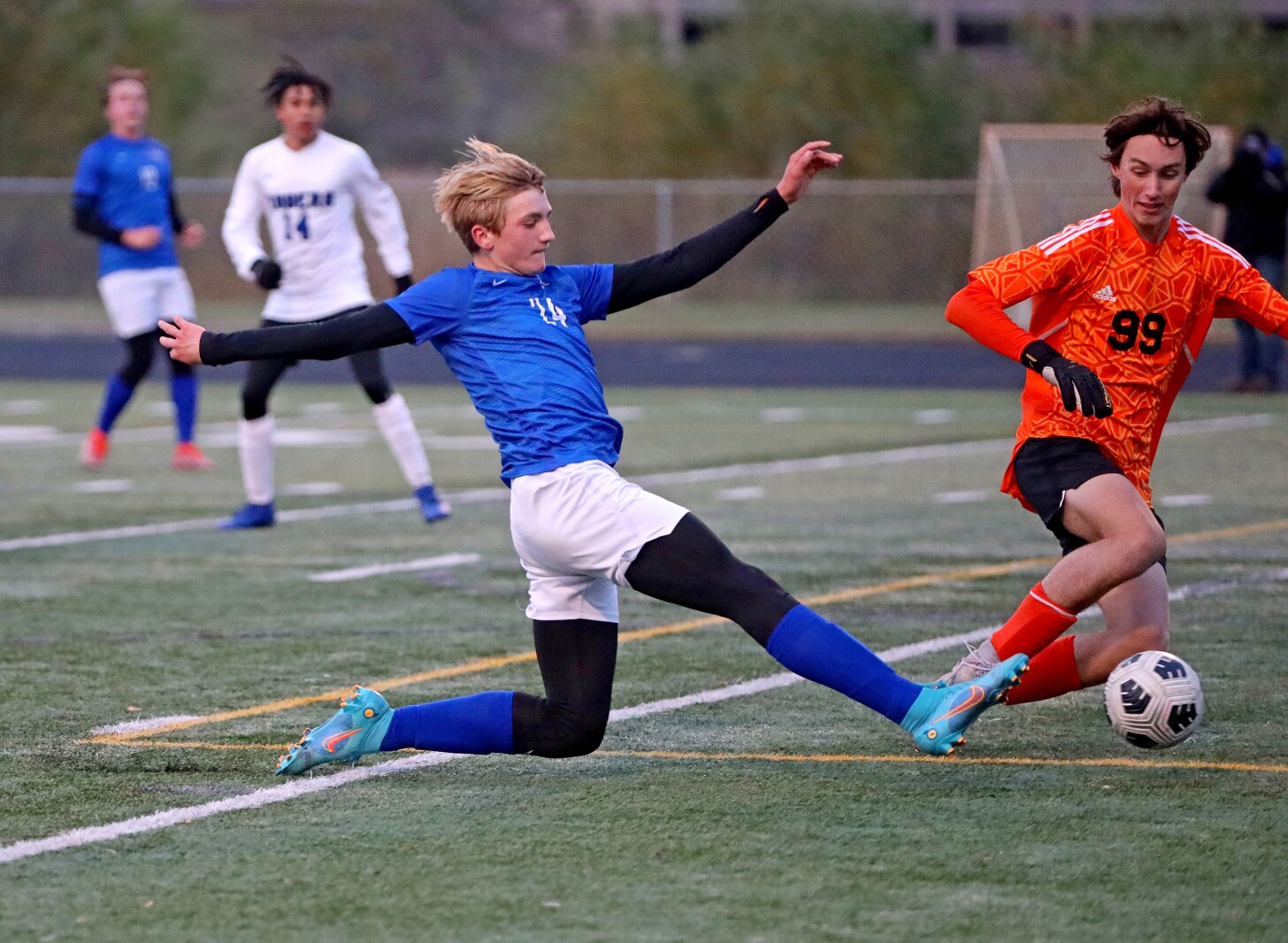 Soccer player stretches to kick the ball as a goalie defends.
