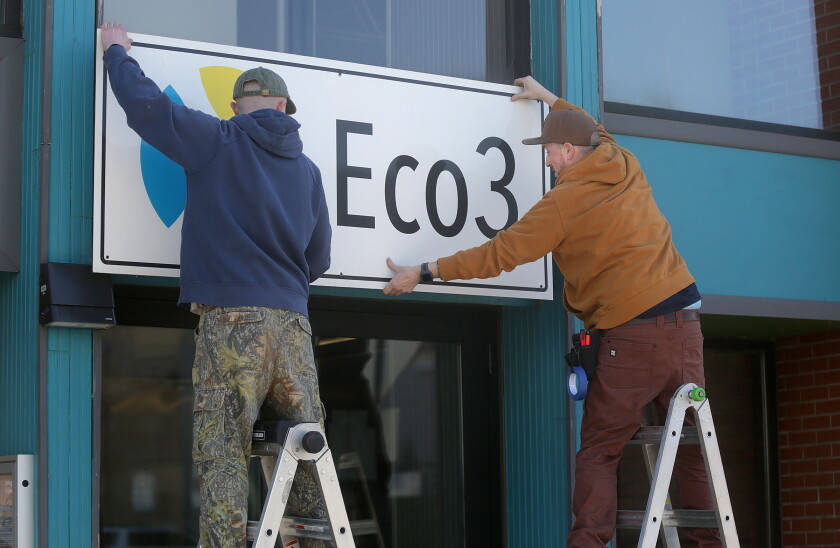 Two men on ladders removing a sign from a storefront.