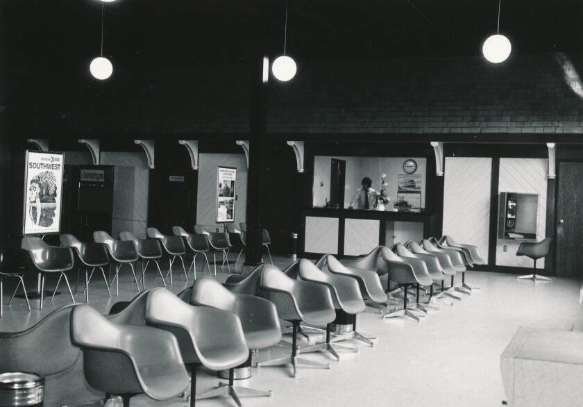 Rows of contoured plastic seats are seen in a train station. Employee works at counter in background.