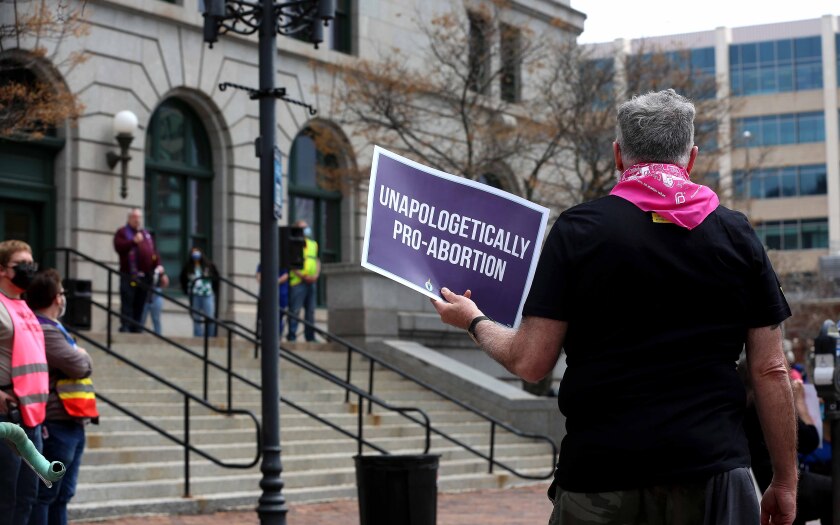 Man holds sign while listening to a speaker at a protest