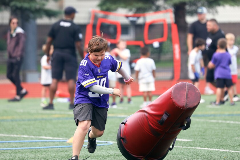 A young boy knocking down a tackling dummy at a youth football camp.