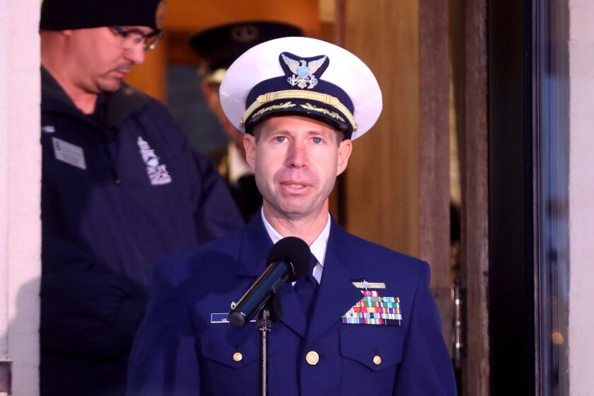 A man wearing a U.S. Coast Guard uniform speaks into a microphone.