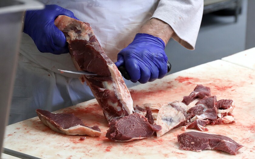 Workers cuts chunks of meat for hamburger for a customer