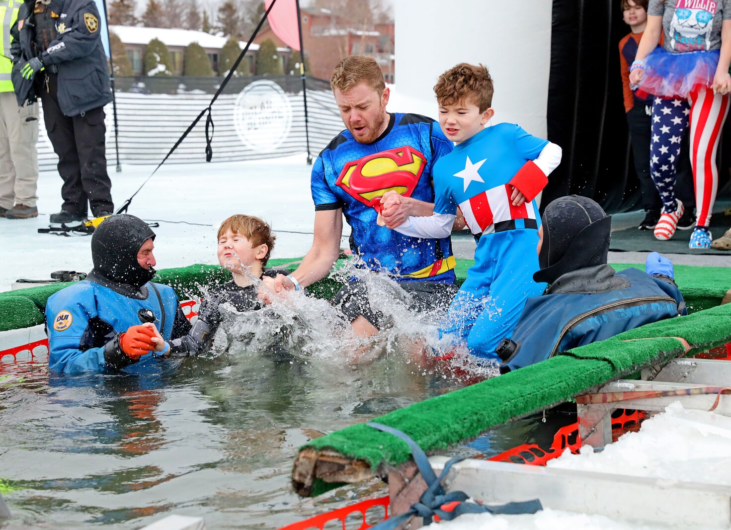A man and two children in superhero costumes enter the water during the Polar Plunge event on Pelican Lake.