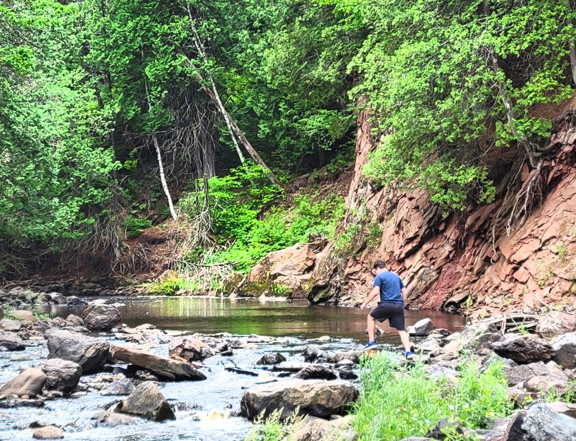 A boy in a blue shirt steps onto rocks to cross the Black River.