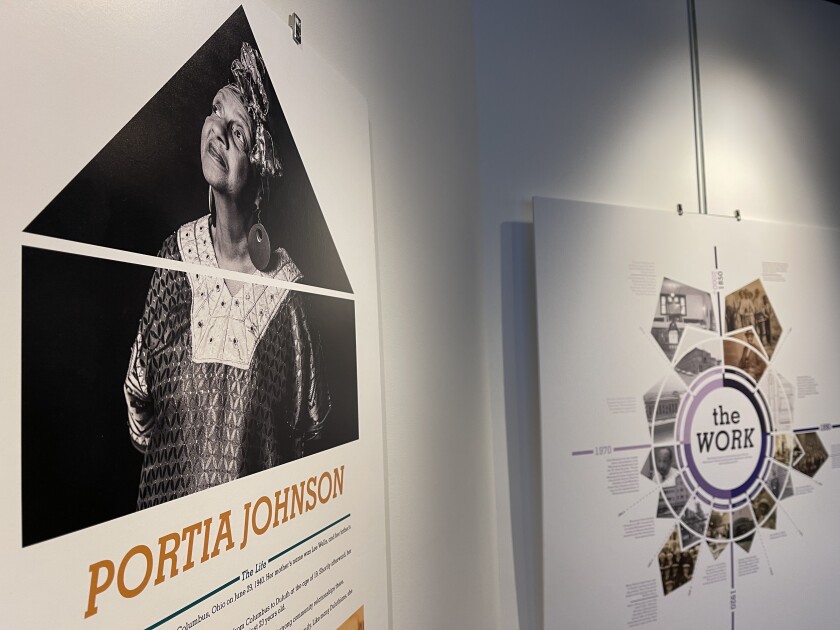 Interior view of historical exhibit. Poster in foreground shows photograph of Black woman and title "Portia Johnson." In background, historical graphic titled "The Work" is seen.