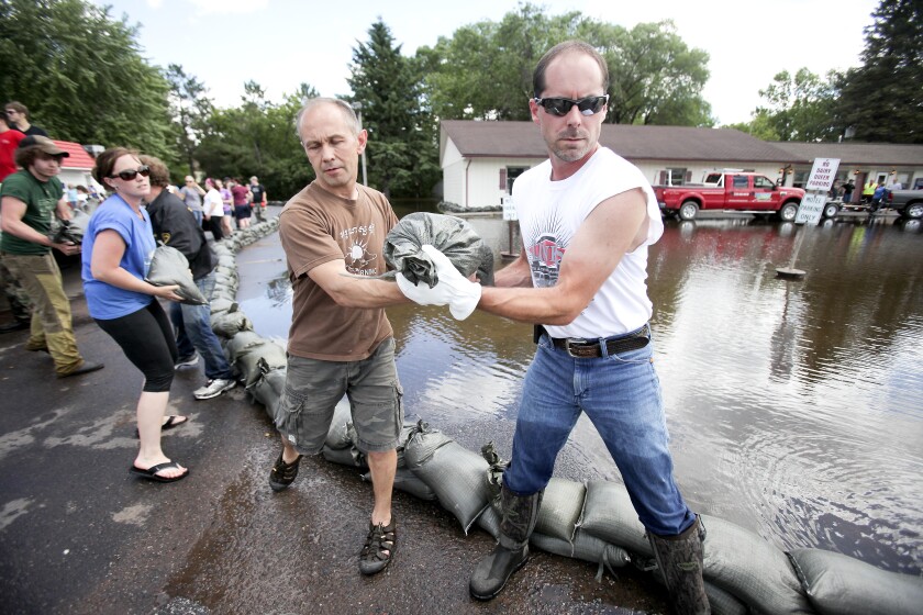 A line of people pass sandbags to stack near a flooded parking lot