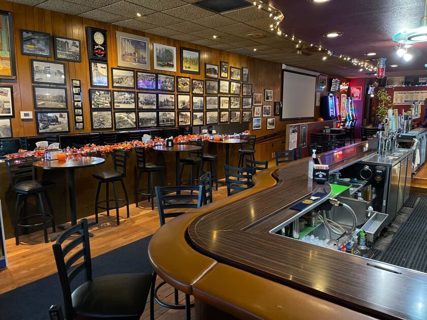 Barroom as seen from next to the bar, with rows of framed black-and-white historical photos visible on opposite wall, behind high-top tables.