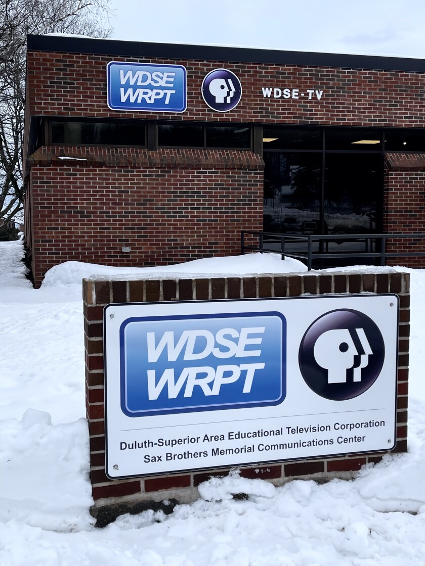 An exterior view of a low, rectangular brick building in a snowy setting. Signage on the building and on a standalone sign indicates WDSE-WRPT with the PBS logo.