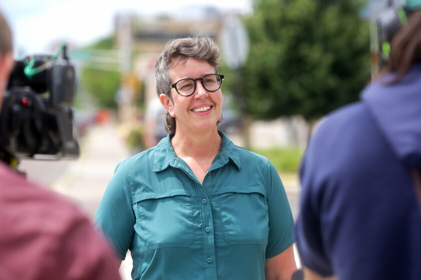 A woman smiling while standing in front of cameras and reporters.