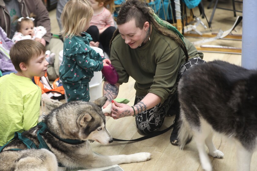 A person putting booties on a dog while children look on during an indoor event.