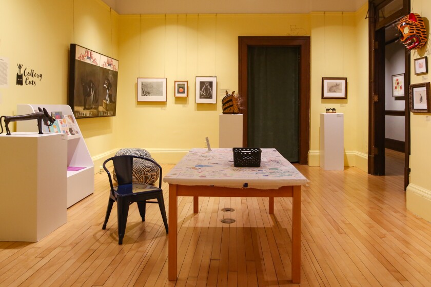 The Rourke nods to its feline history with a show featuring cats in its children's gallery. Organization founder James O'Rourke had a history of keeping cats in the original gallery, and cats are a common theme in Rourke shows and art. A room with yellow walls and wood floors. There is a rectangular table in the middle of the room. It has a sheet of paper covering it that people can draw on. There are other art pieces on the walls.
