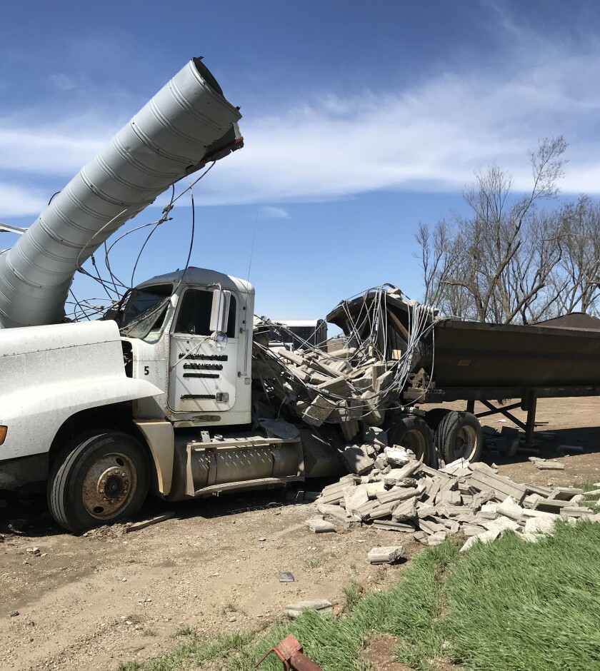 A grain truck and trailer are damaged by a wind storm that tore grain bins from their moorings.