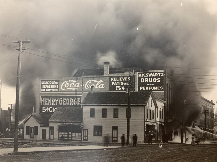 Pedestrians watch from the street as water is sprayed on a burning building as smoke billows high in the sky.