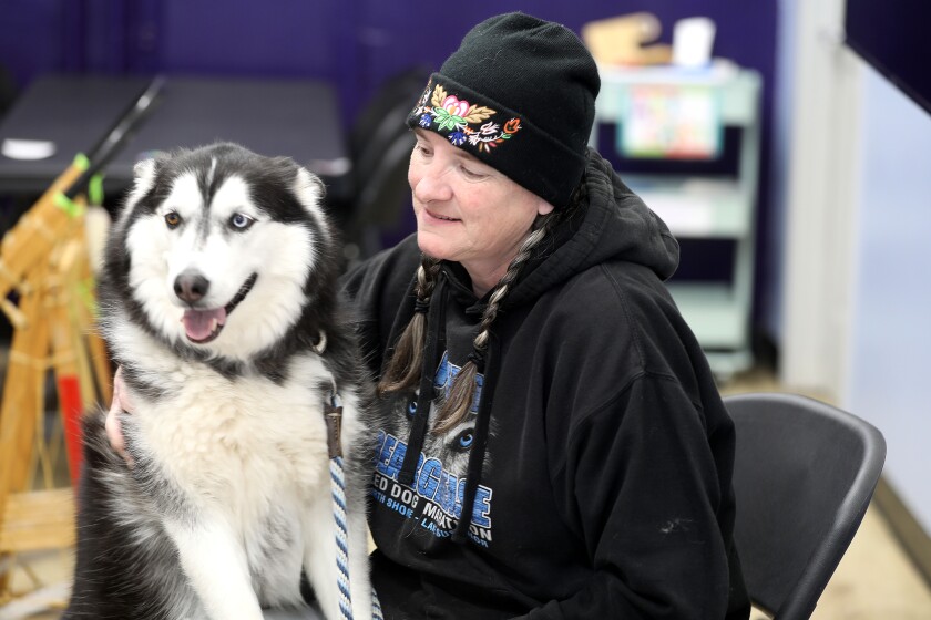A woman sitting with her dog at an indoor event.