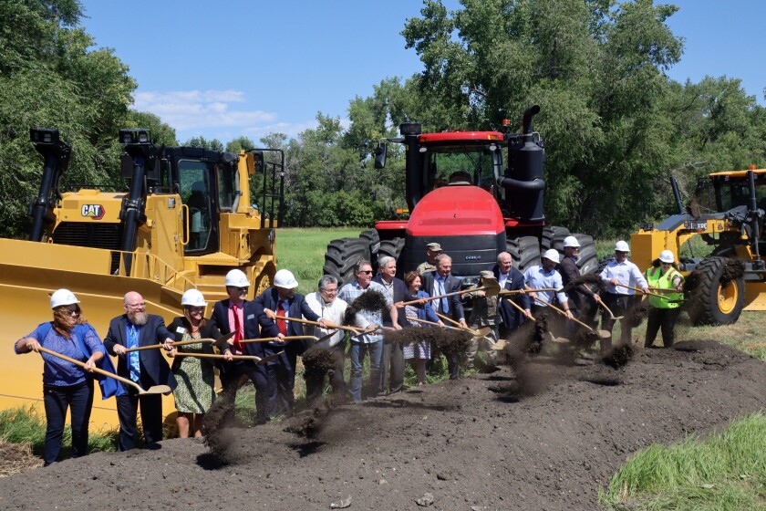 More than a dozen people shovel dirt together.
