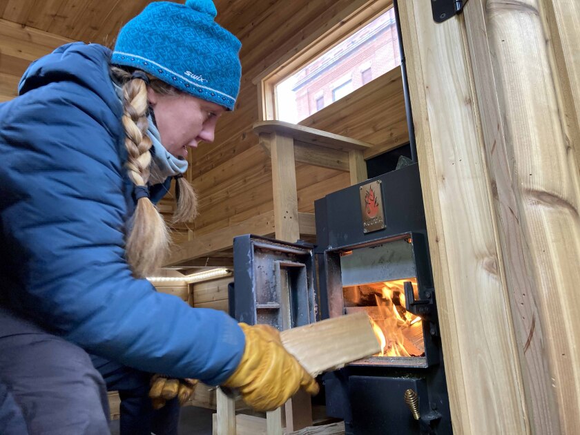 A woman adds wood to a stove inside of a sauna