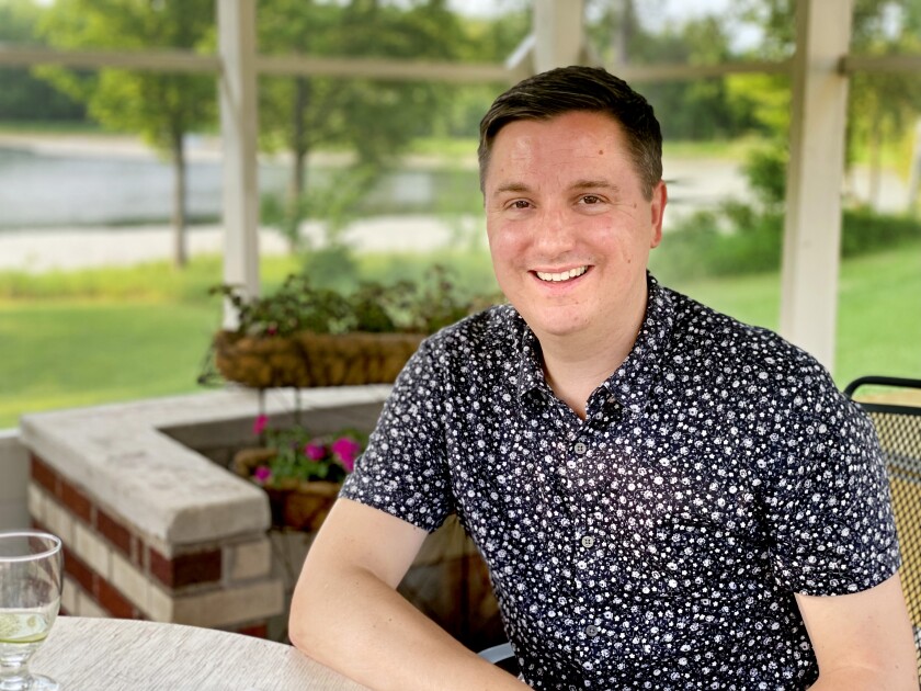 Tom DeCaigny poses for a photo outside the Historic Scott House in Carlton. There are green grounds behind him and a nearly empty glass of wine on the table next to him.