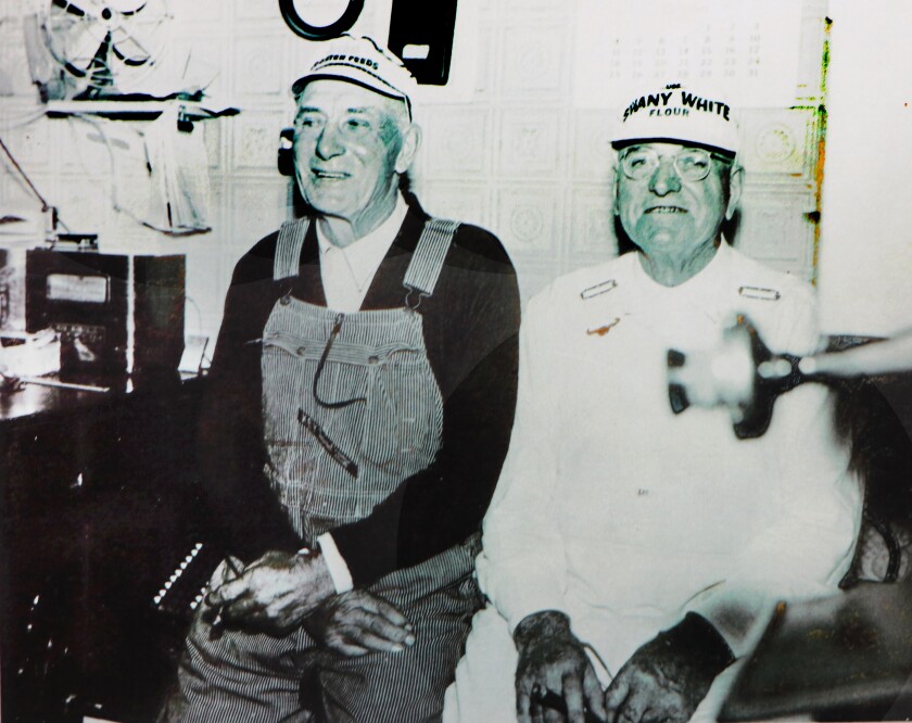 Two brothers in flour mill clothes smile for a camera. A crank telephone microphone is at right.