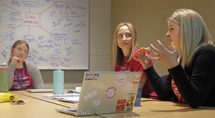 Three women in red shirts and straight shoulder-length hair sit around a conference table.