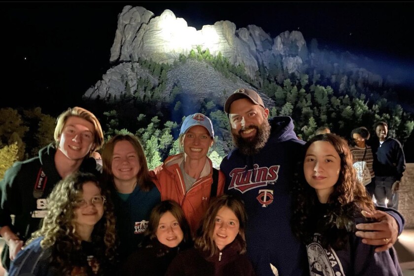 Two adults and six children pose in the foreground of Mount Rushmore.