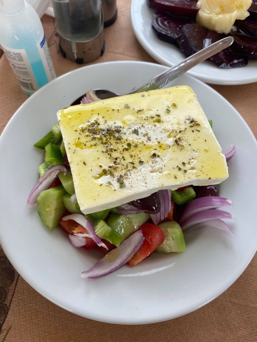 A slab of feta cheese drenched in olive oil and herbs rests atop a vegetable salad.