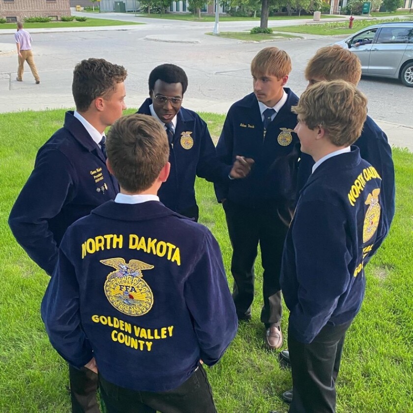 FFA members in blue FFA jackets gather on a yard in a circle and talk.