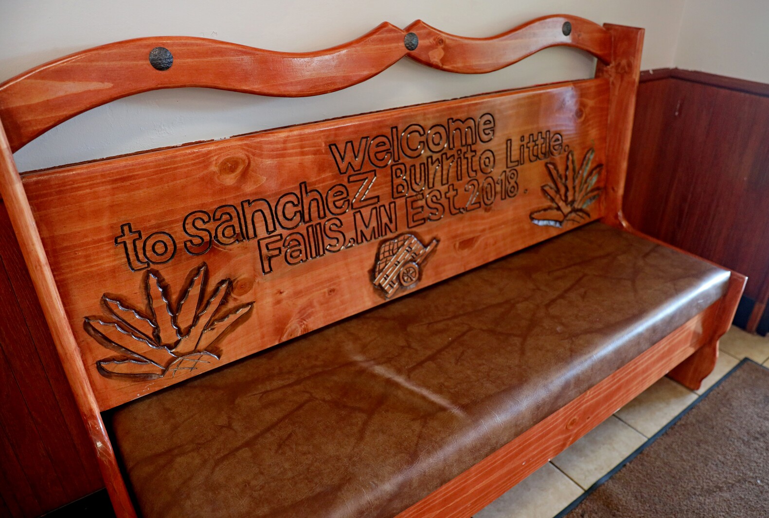 Wooden, hand-carved bench says "Welcome to Sanchez Burrito, Little Falls, MN, Est. 2018