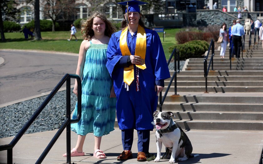 A graduate, a young girl and a dog pose for a photo