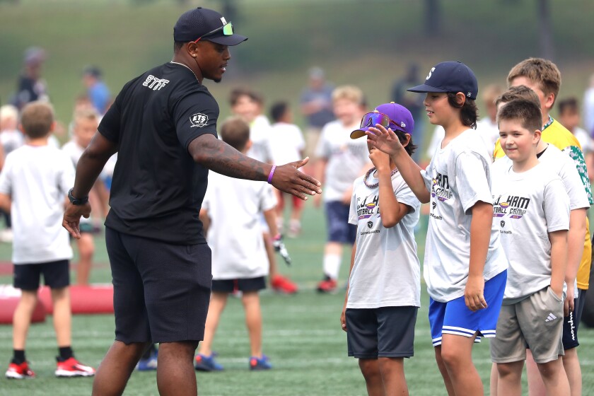 A pro football player slapping hands with kids at a youth camp.