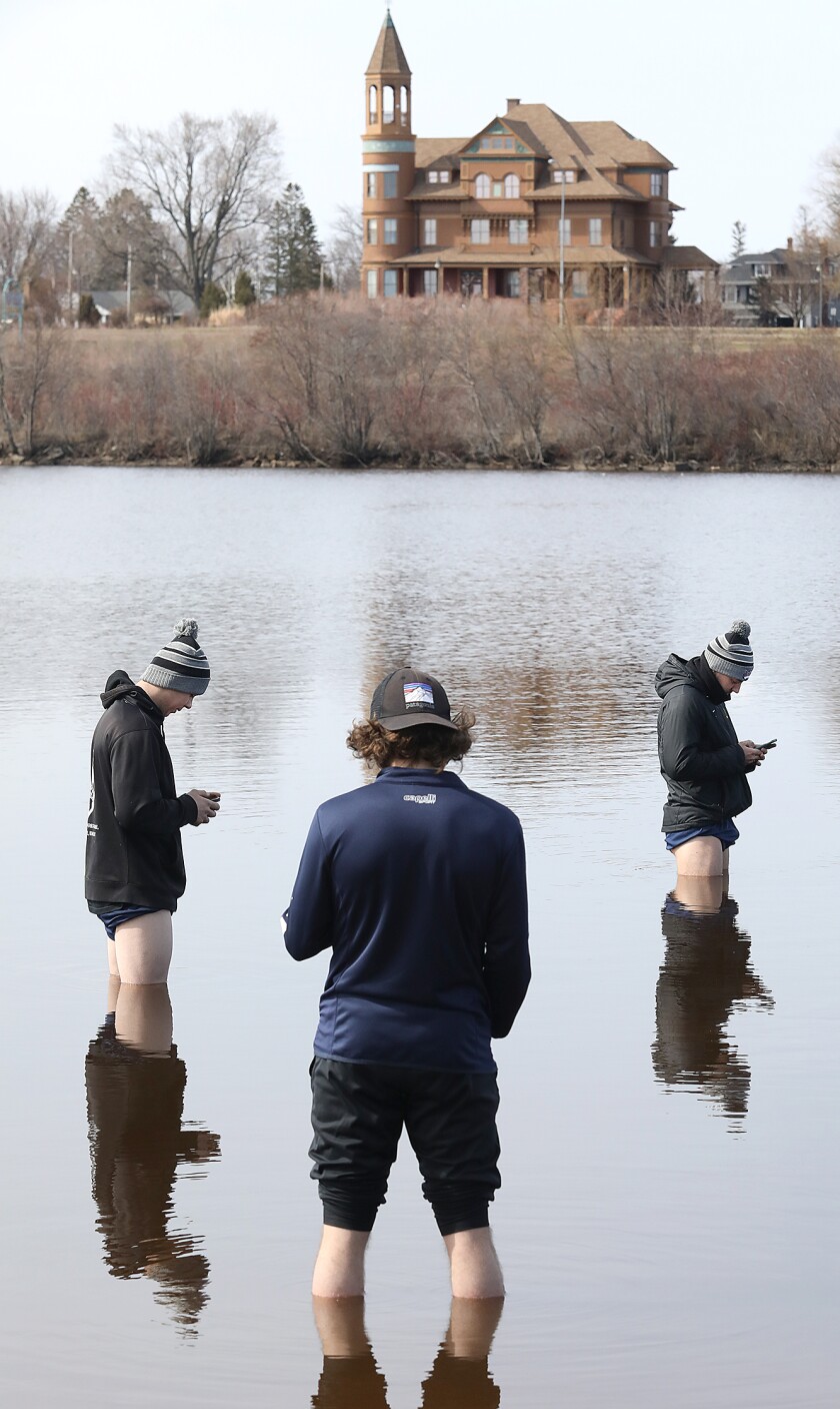 Alex Paredes, left, Blake Perry, center, and Scott Wilson stay bundled up as they look at their phones while they stand in the frigid waters of the Superior Bay